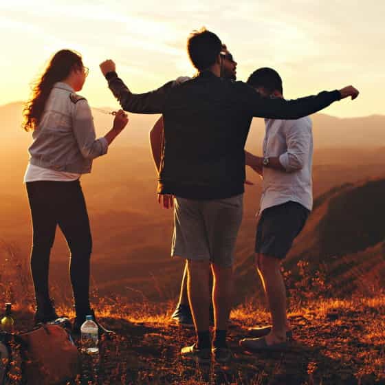 Groupe d’amis profitant d’un coucher de soleil en pleine nature, partageant un moment de convivialité sur un sommet avec vue panoramique.