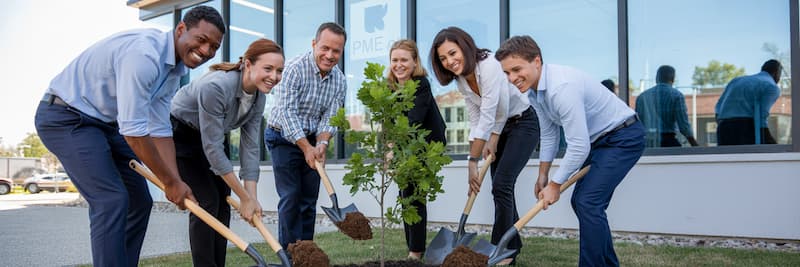 Un chef d’entreprise et ses salariés plantant
symboliquement un arbre devant les locaux de la PME. Tous sourient et participent, symbolisant le lancement collectif d’une démarche écoresponsable au sein de l’entreprise.